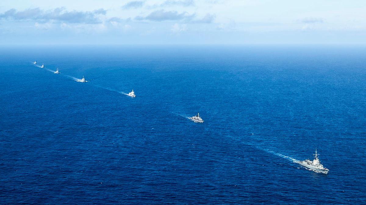 Seven ships sail in a line in a deep blue ocean.