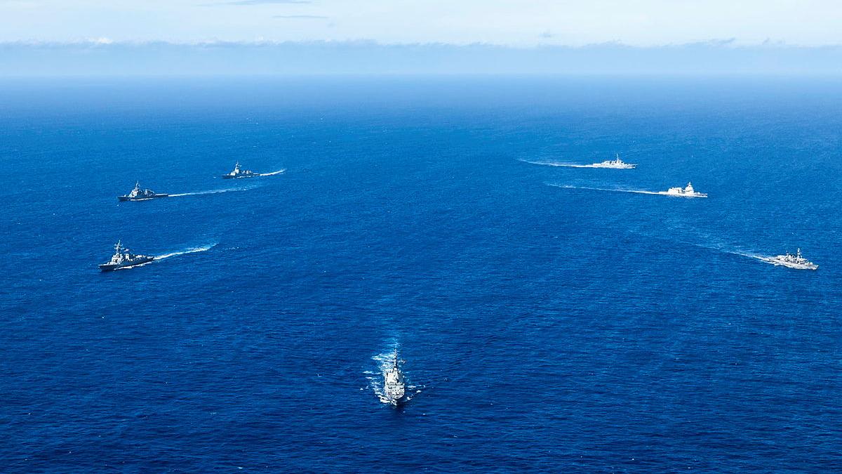 Seven ships sail away from each other out at sea.