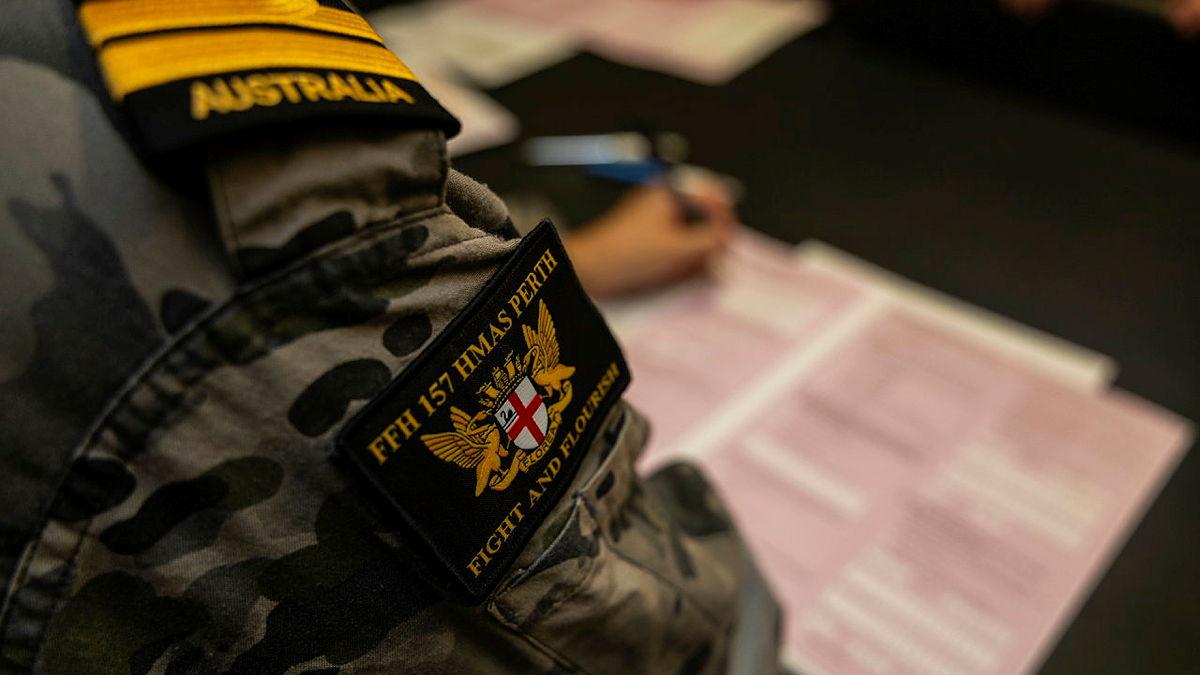 The shoulder and arm of a navy officer is seen as they write on a form.