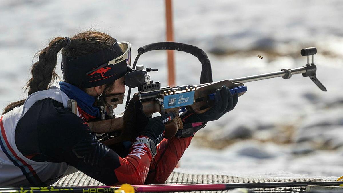 A woman holds a rifle and takes aim in snow covered terrain.