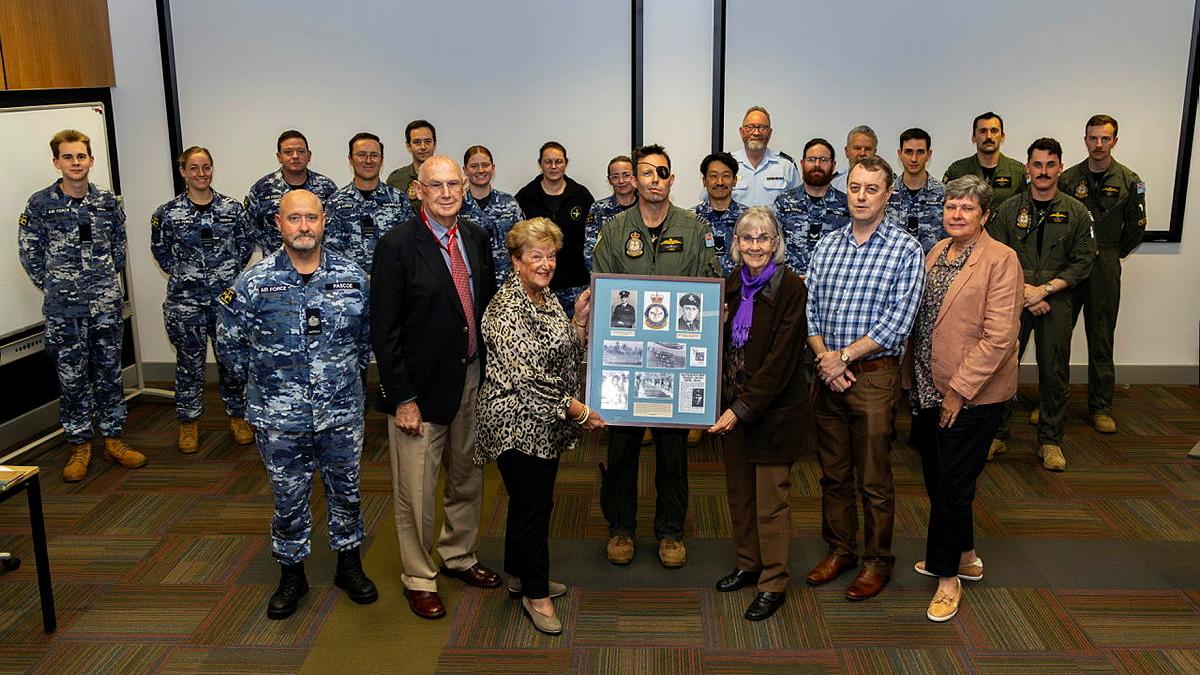 A group of military personnel and civilians stand in a group with a large blue plaque.