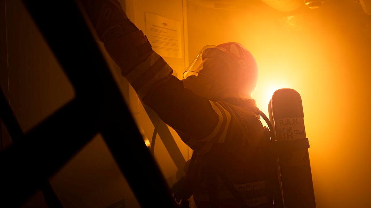 A person in protective firefighting gear prepares to climb a ladder in a room filled with and orange glow.