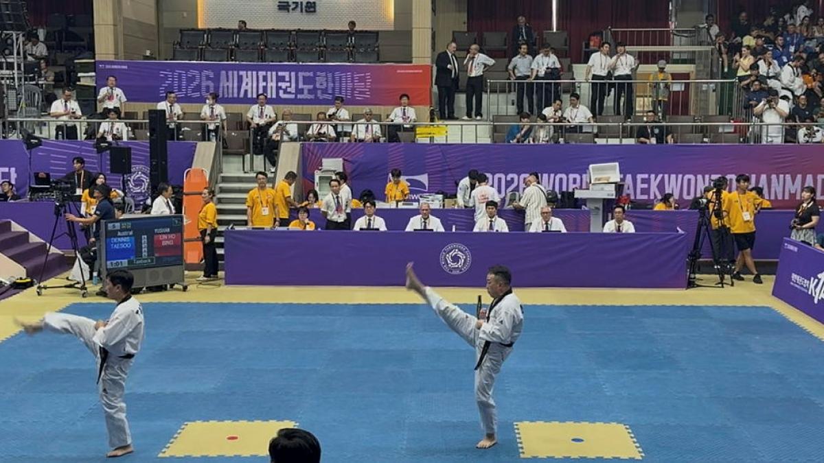 Two men perform high kicks in an arena.