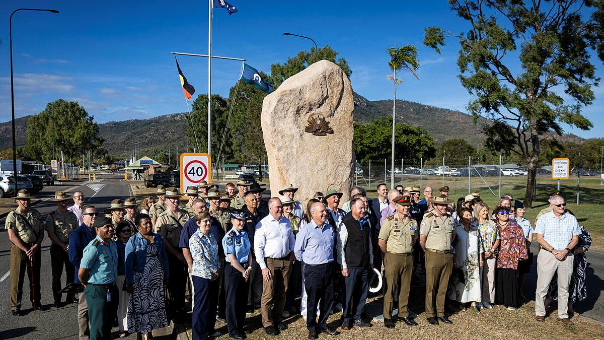 A group of people stand in front of a large rock.