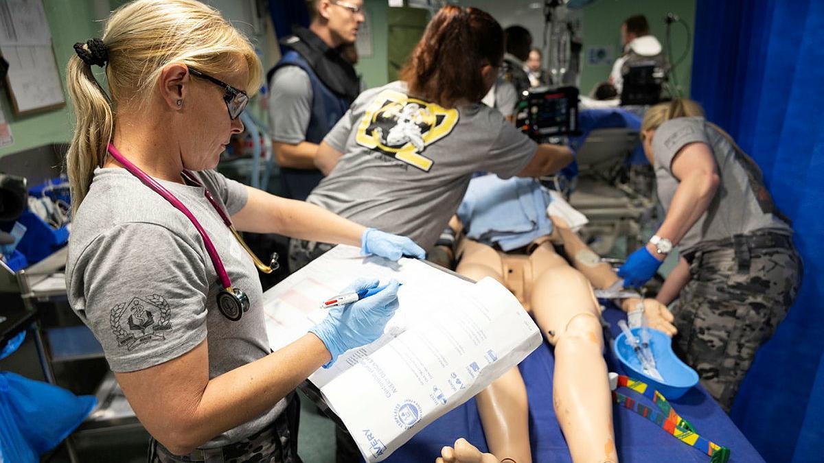 A group of medical people work together on a mock patient.