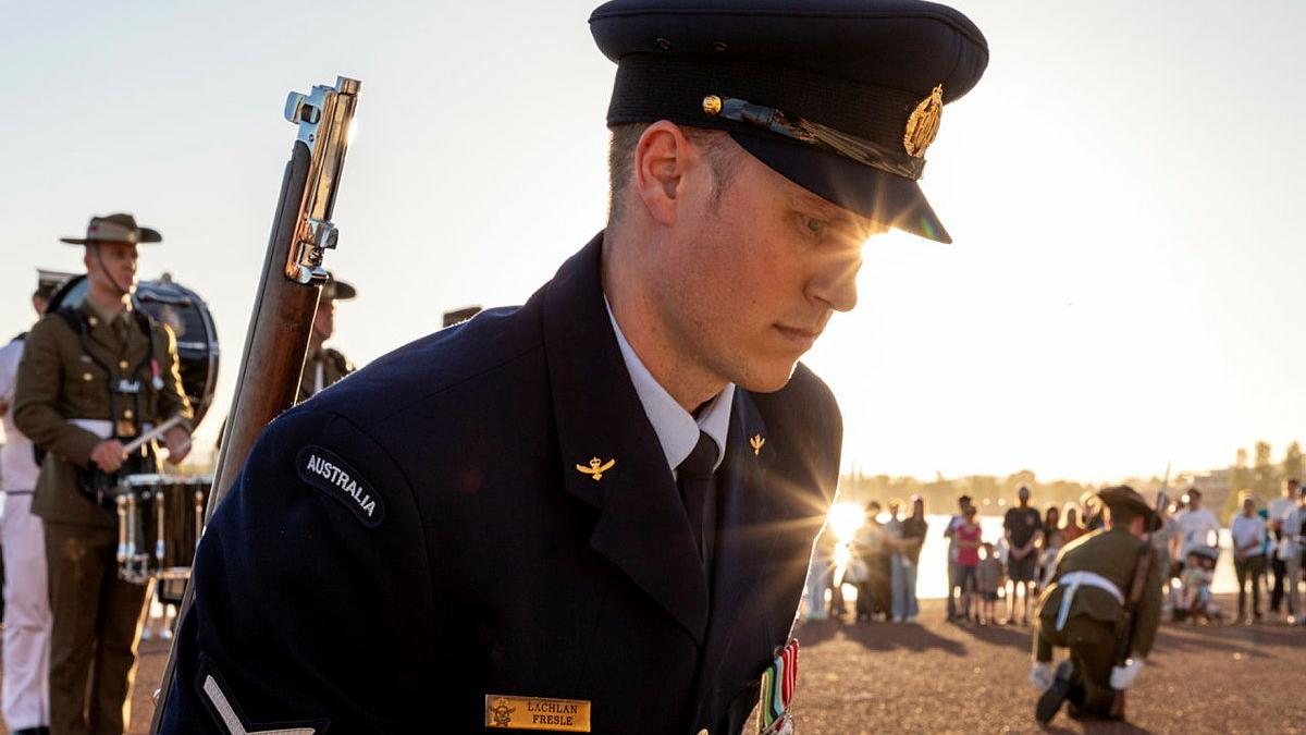 A military man kneels with others at sunrise.