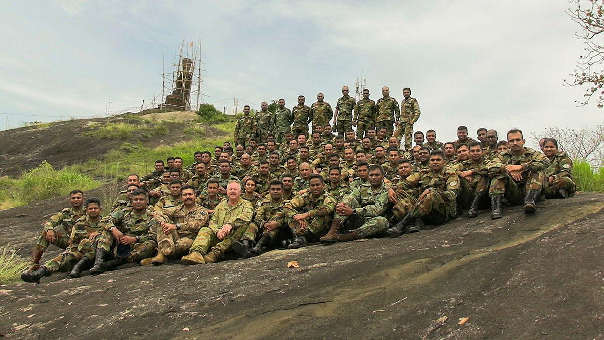 A large group of military personnel sit on a rocky cliffside.