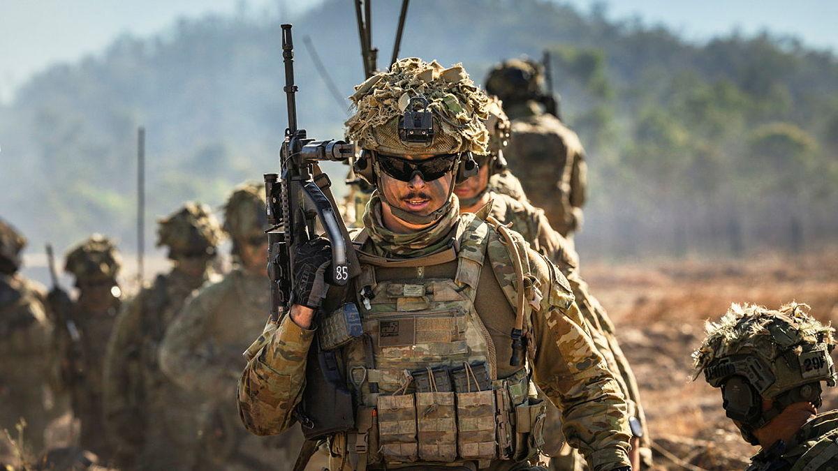 Australian Army soldiers holding their guns and walking across country