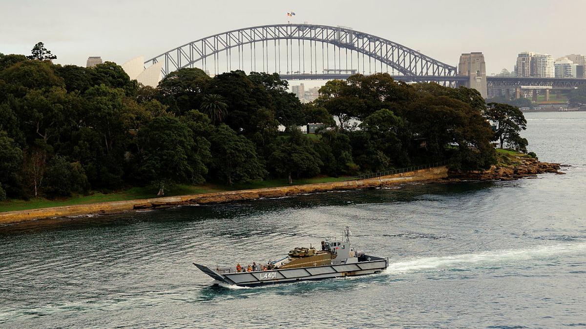 A ship sails through a harbour with a bridge in the background.