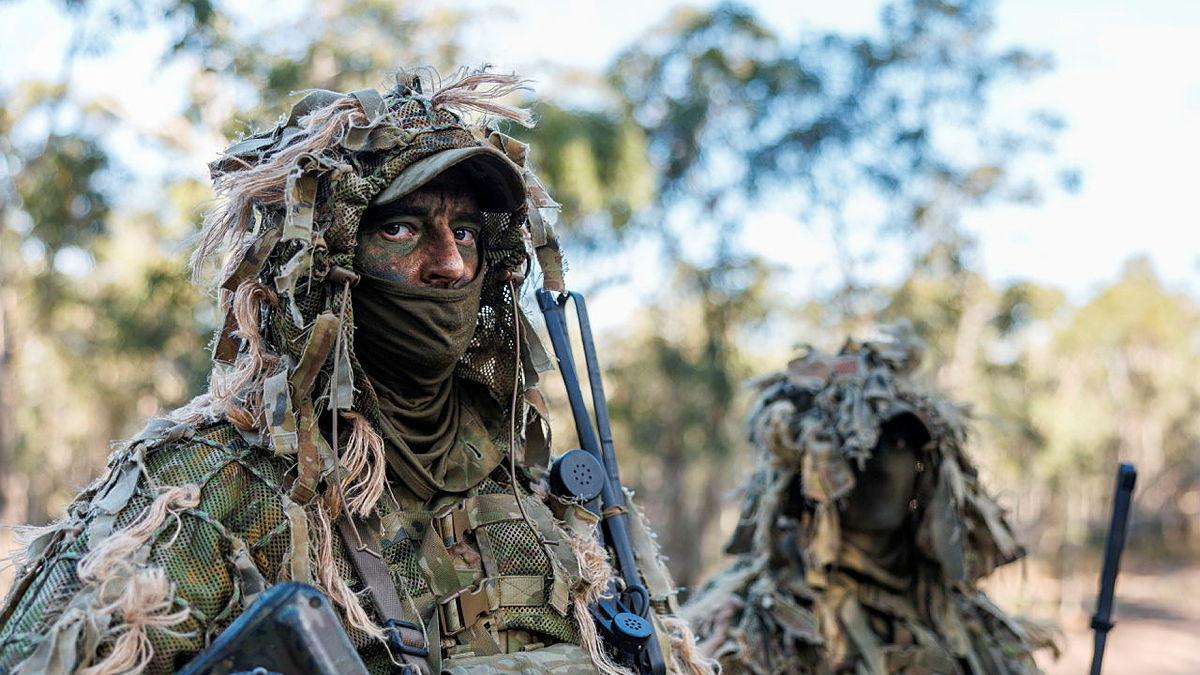 Two Army soldiers covered in camouflage face the camera with serious looks on their faces.