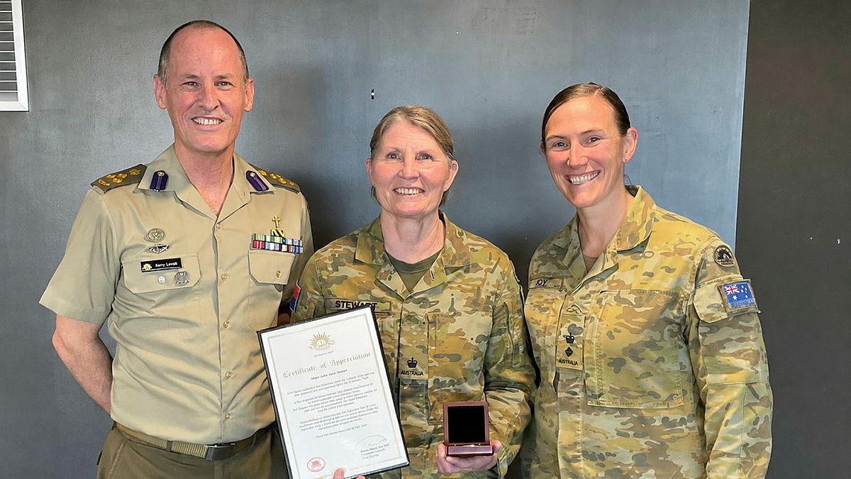 Three Army leaders stand together facing the camera with one member holding an award that recognises 40 years of service.