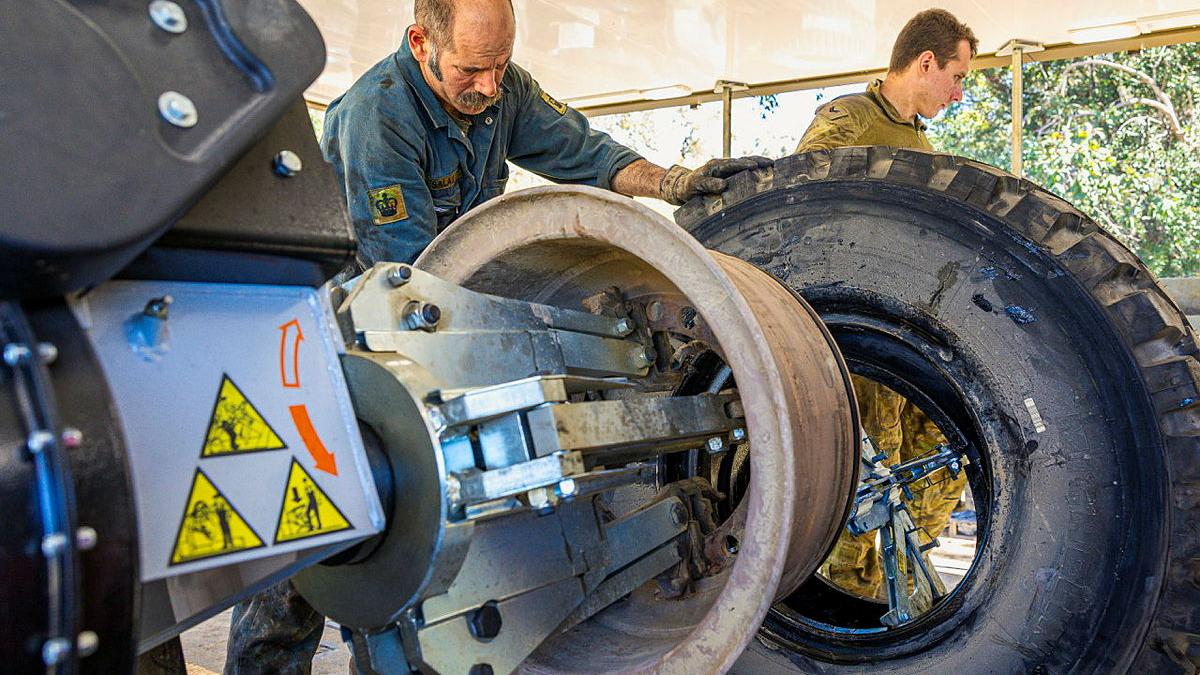 Warrant Officer Class Two Shayne Salau, and Corporal Keegan Pearse, inside the tyre-changing station, operating machinery to change a flat tyre.