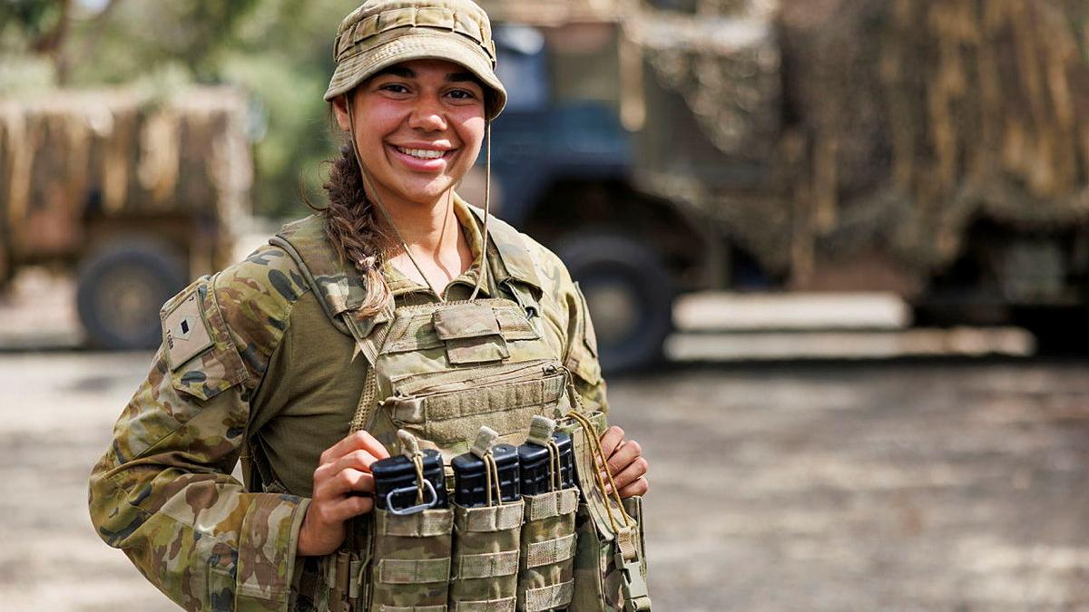 A female soldier stands, smiling, with items tucked into her uniform pockets.