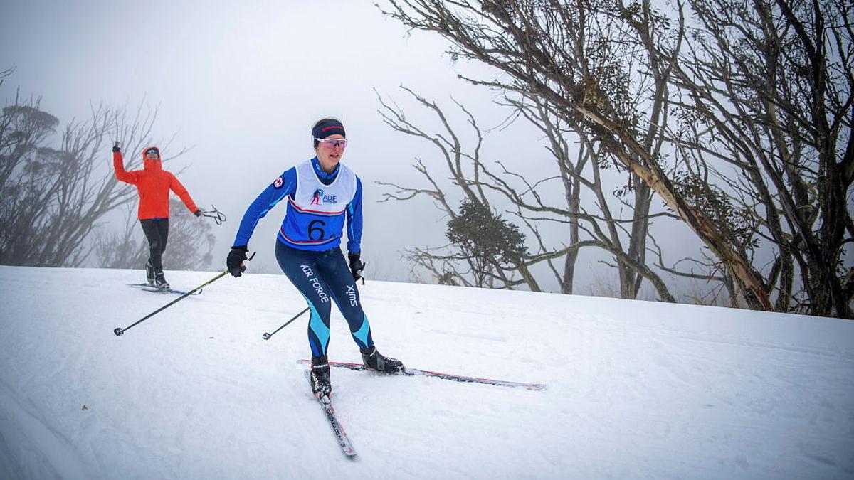 An Air Force woman on skis paces another skier in an orange coat on the slopes.