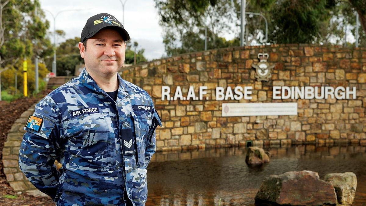 Portrait of Royal Australian Air Force Avionics Technician Sergeant Lee O’Regan, in uniform standing in front of RAAF Base Edinburgh entrance.
