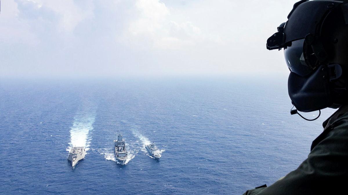 A person in a helmet looks down at three ships on the ocean.