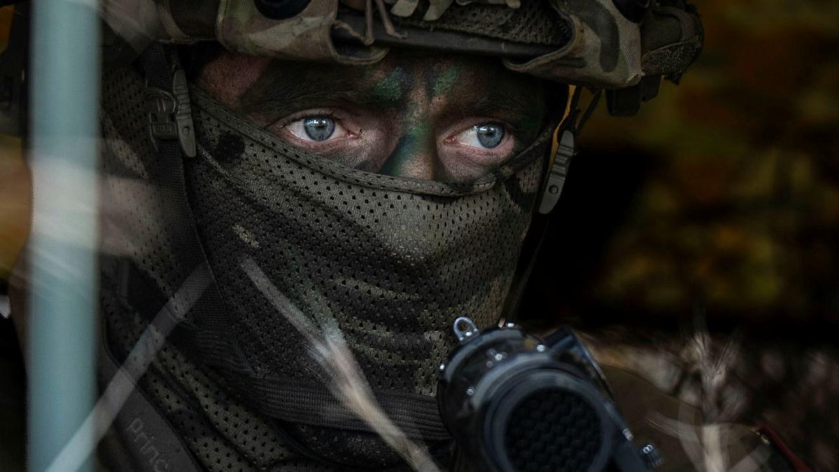 A soldier in full military gear waits in hiding.