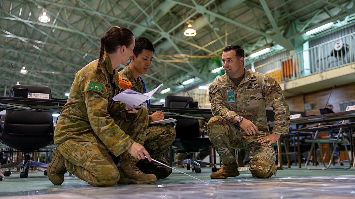 Three military members work together while knelt on the floor.