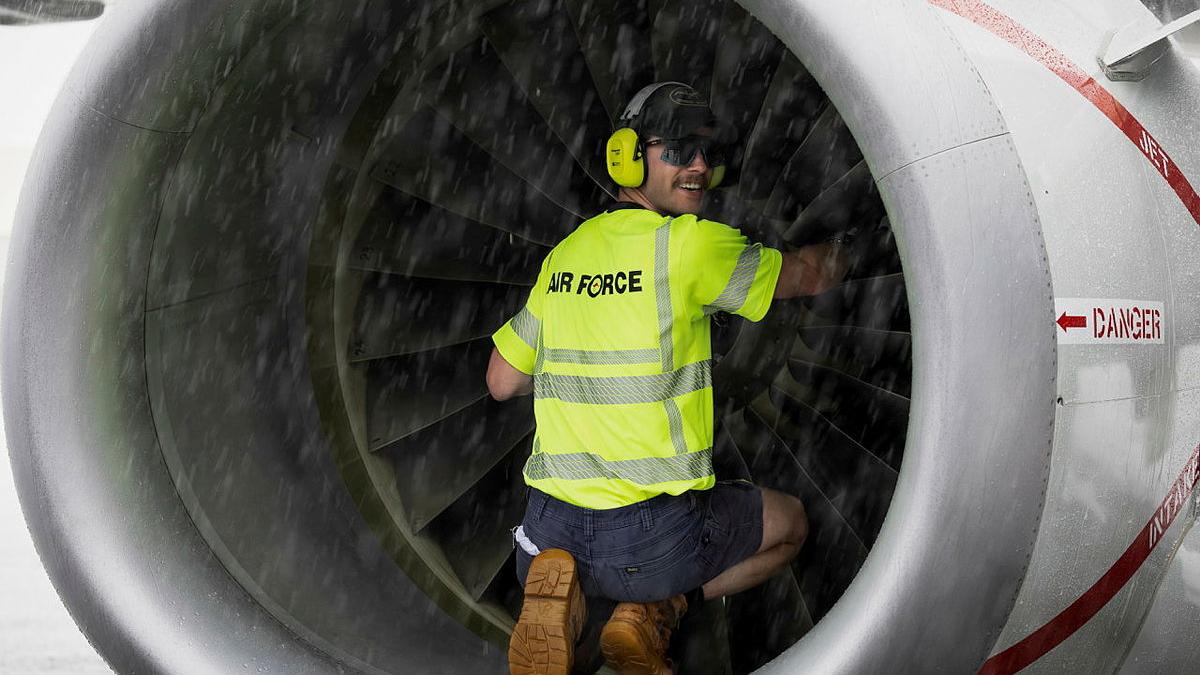 A man in yellow Air Force branded clothing and ear protection sits inside a cylindrical part of an aircraft .