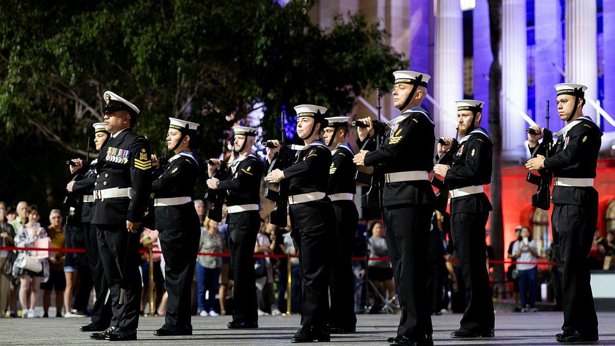 A group of Navy personnel in black uniforms stand holding firearms.
