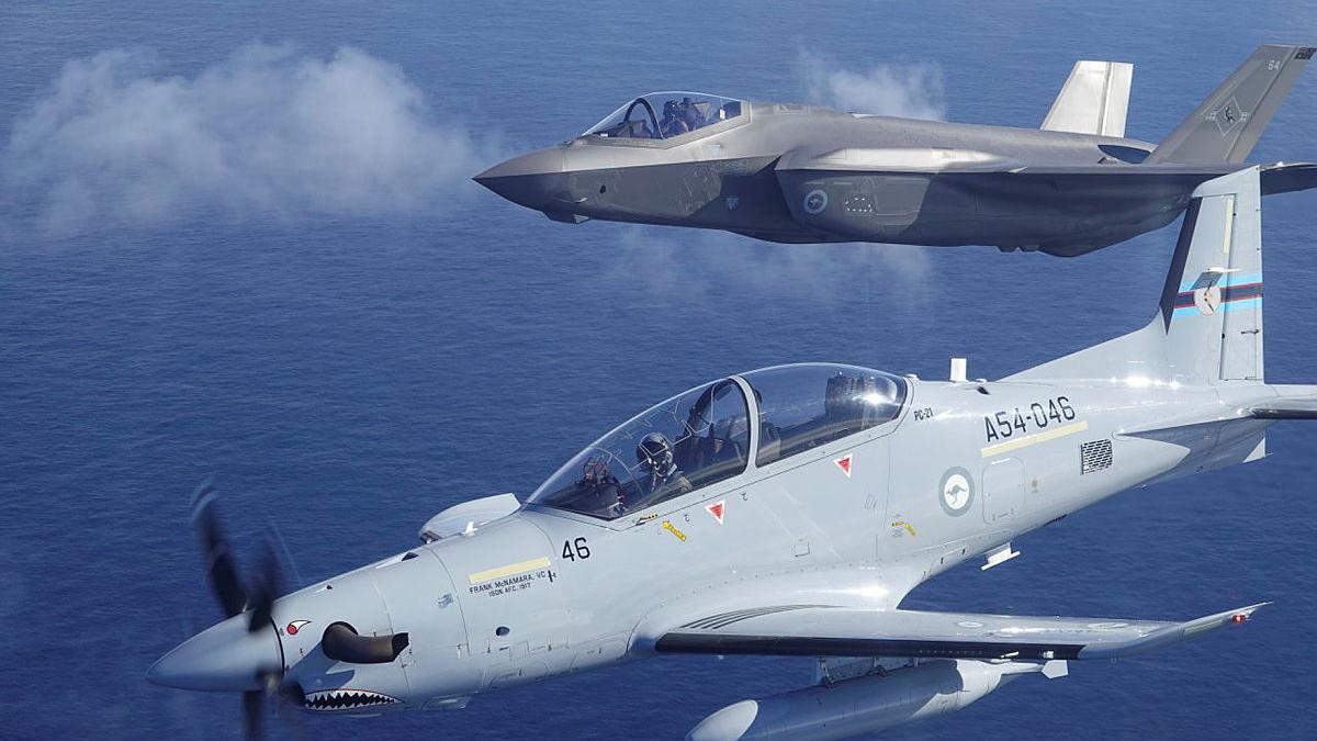 Two different aircraft fly close together in a mostly clear sky.