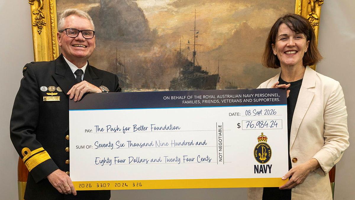 A military man and a civilian woman hold a cheque for The Push for Better Foundation