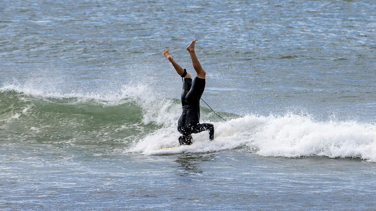 A male surfer does a headstand while surfing in the ocean.