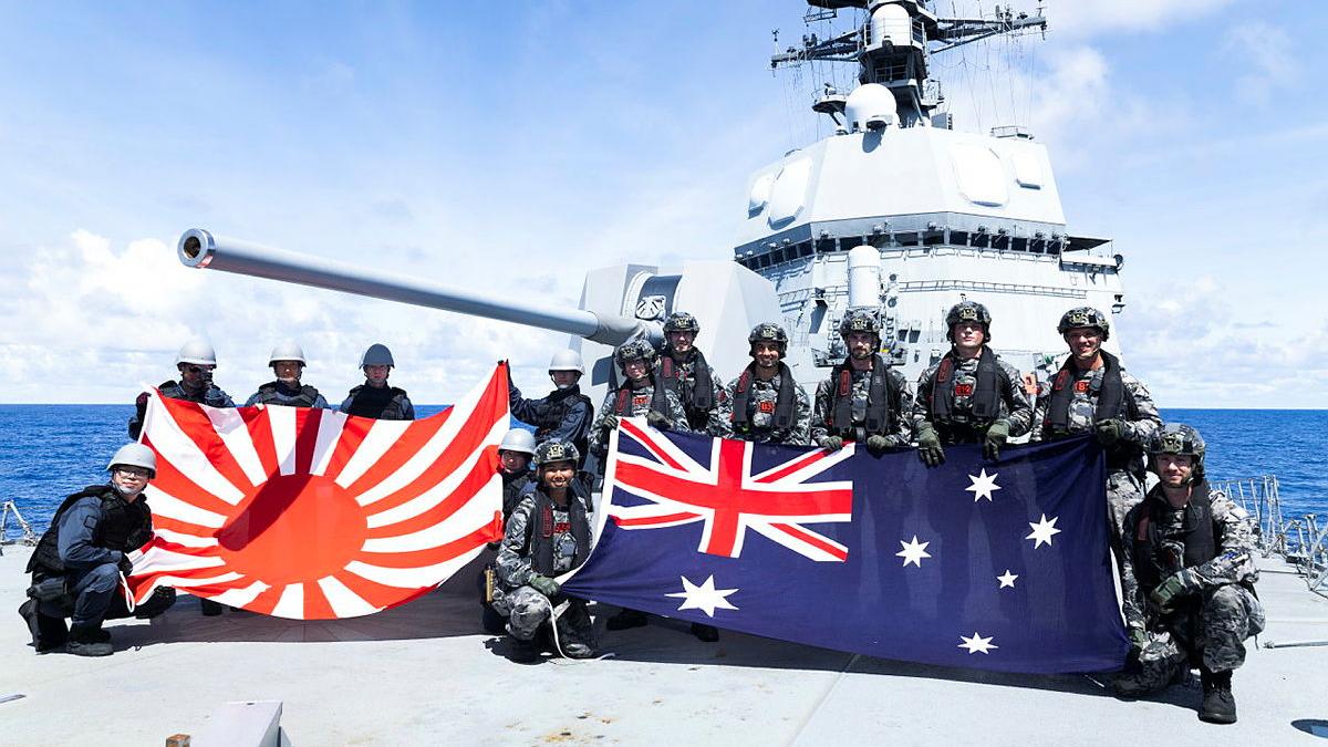Two groups of military members hold a Japanese flag and an Australian flag while on a ship at sea.