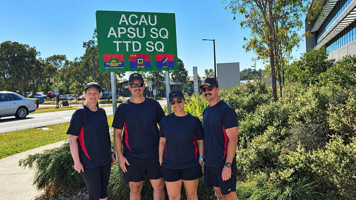 A group of men and women in matching tops stand before a sign reading 'ACAU APSU SQ TTD SQ'.