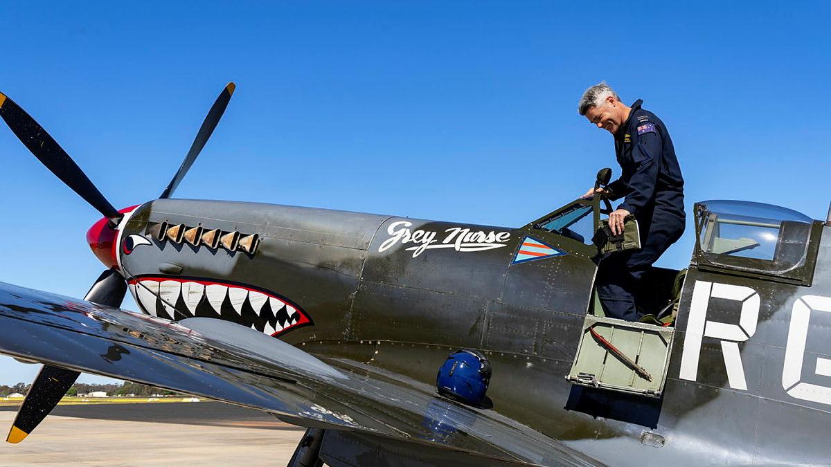 A man stands up to exit from the cockpit of a small aircraft that has eyes and teeth painted on it.