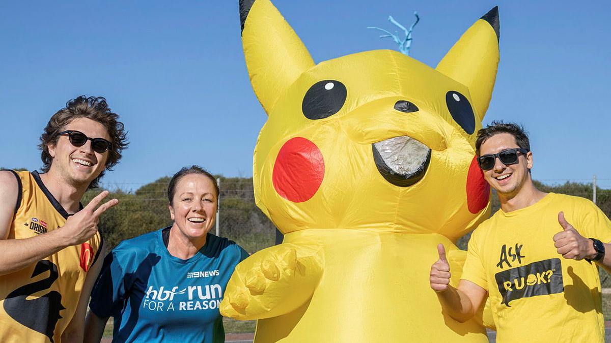 A inflatable yellow cartoon mascot stands with three people in exercise gear.