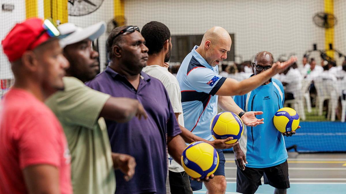 A group of men stand in a line, all holding a bright yellow and blue ball out in front of them.