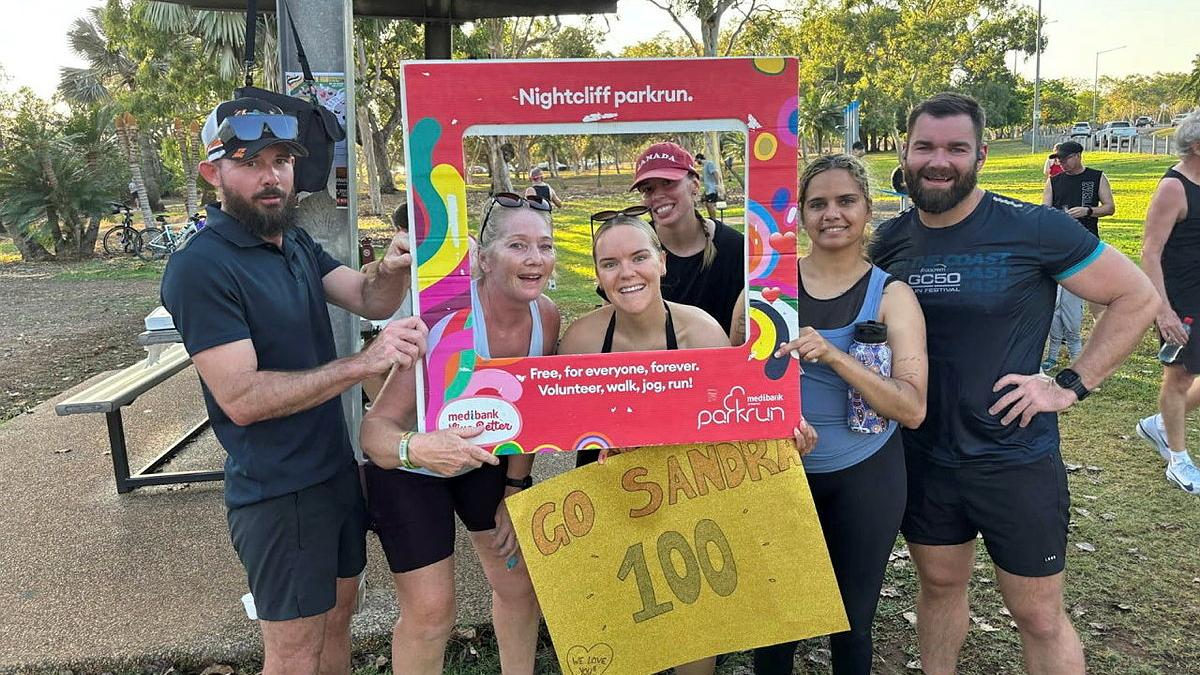 A group of people in exercise gear crowd around a large colourful square frame to look like they are in a photo.