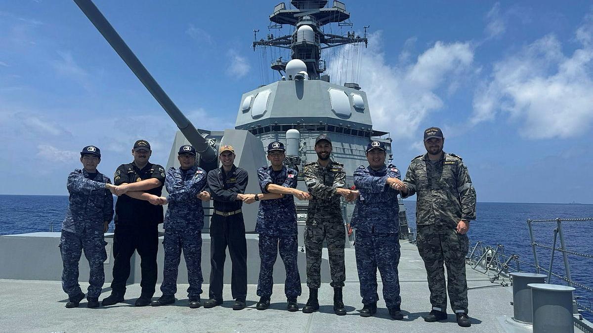 A group of military personnel stand in a line with their arms crossed and holding hands with each other, in a chain.