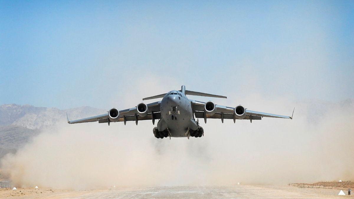 An aircraft takes off from a dirt airstrip. 