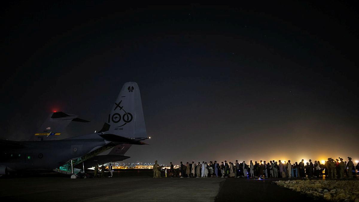 A long line of people wait to board an aircraft at night