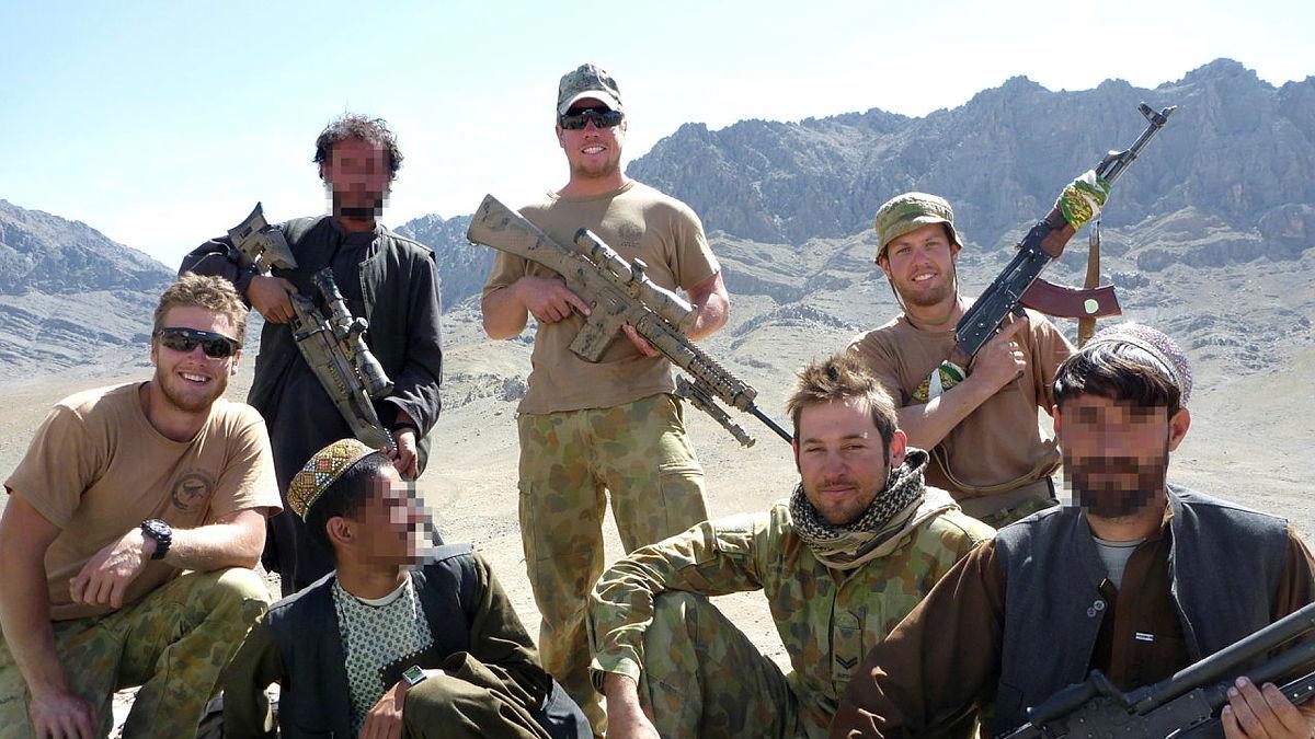 A group of armed soldiers and civilians in a dry, mountainous region.