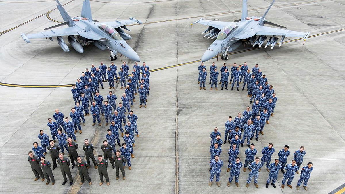 A group of military personnel use their bodies to spell 82 in front of two aircraft.