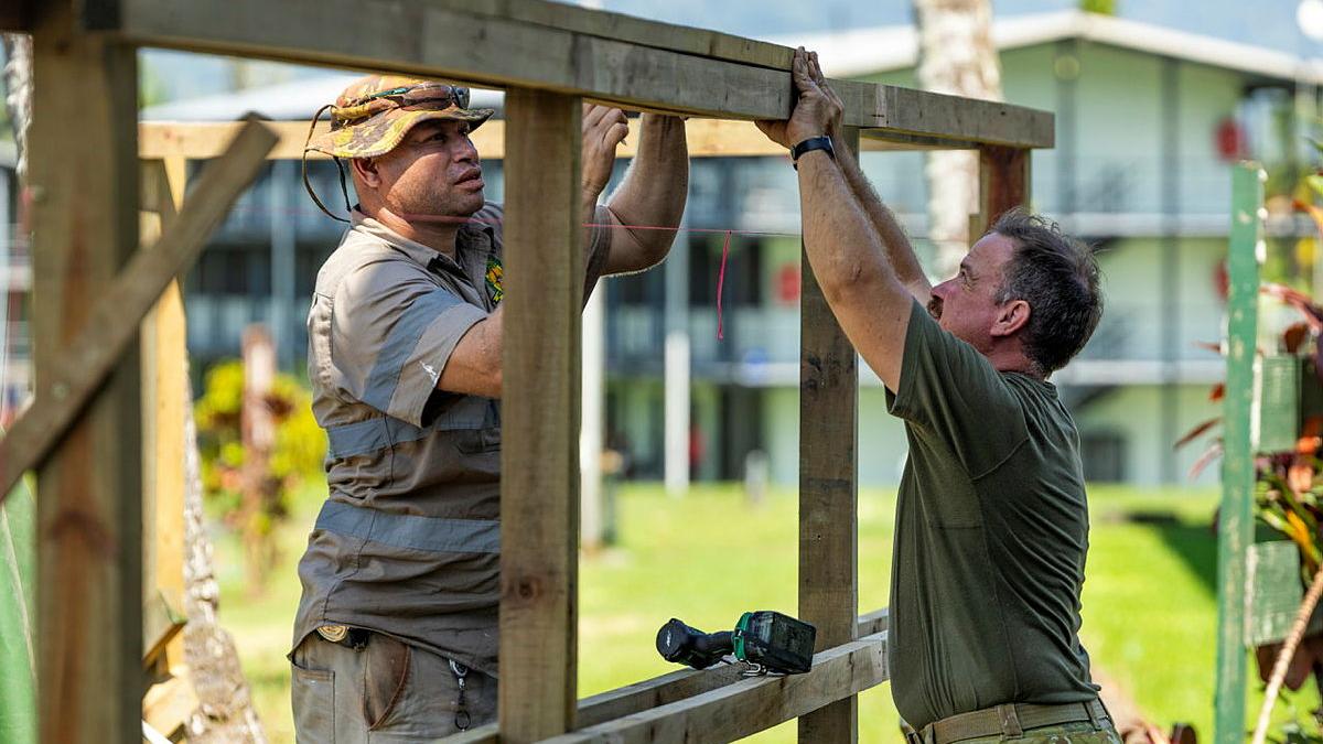 Two men working on a timber frame outdoors.