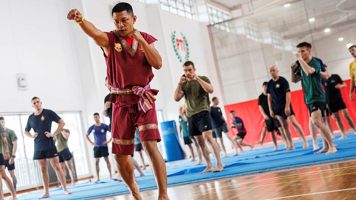 A Thai Army martial artist faces the camera and throws a punch in front of his class.