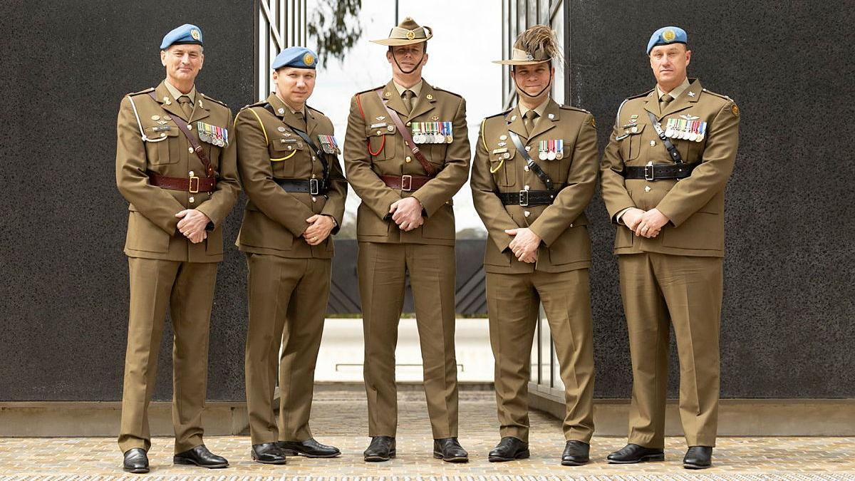 Five men in formal Army uniform stand side by side, three wearing blue peacekeeper berets.