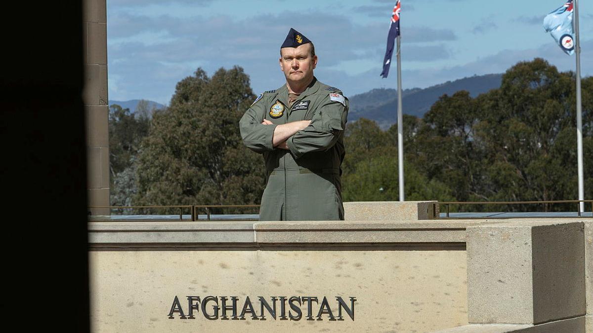 A military man stands with his arms crossed in front of a concrete block with the word 'Afghanistan' on it.