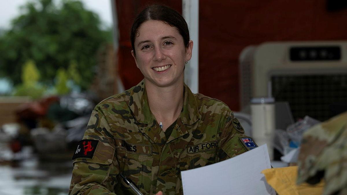 A woman in military uniform holds paper and a pen.