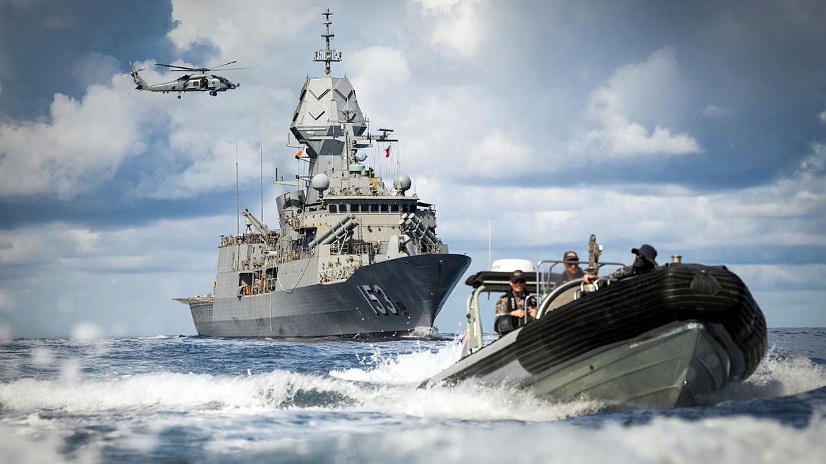 A small boat drives away from a large ship and helicopter at sea.