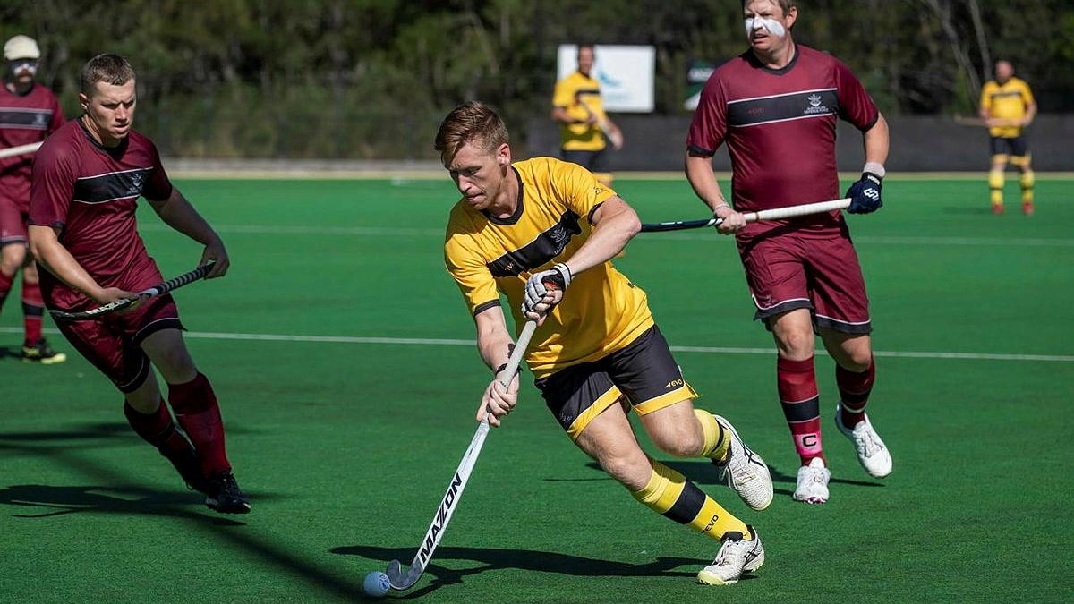 A hockey player in yellow runs the hockey ball past his opponents.