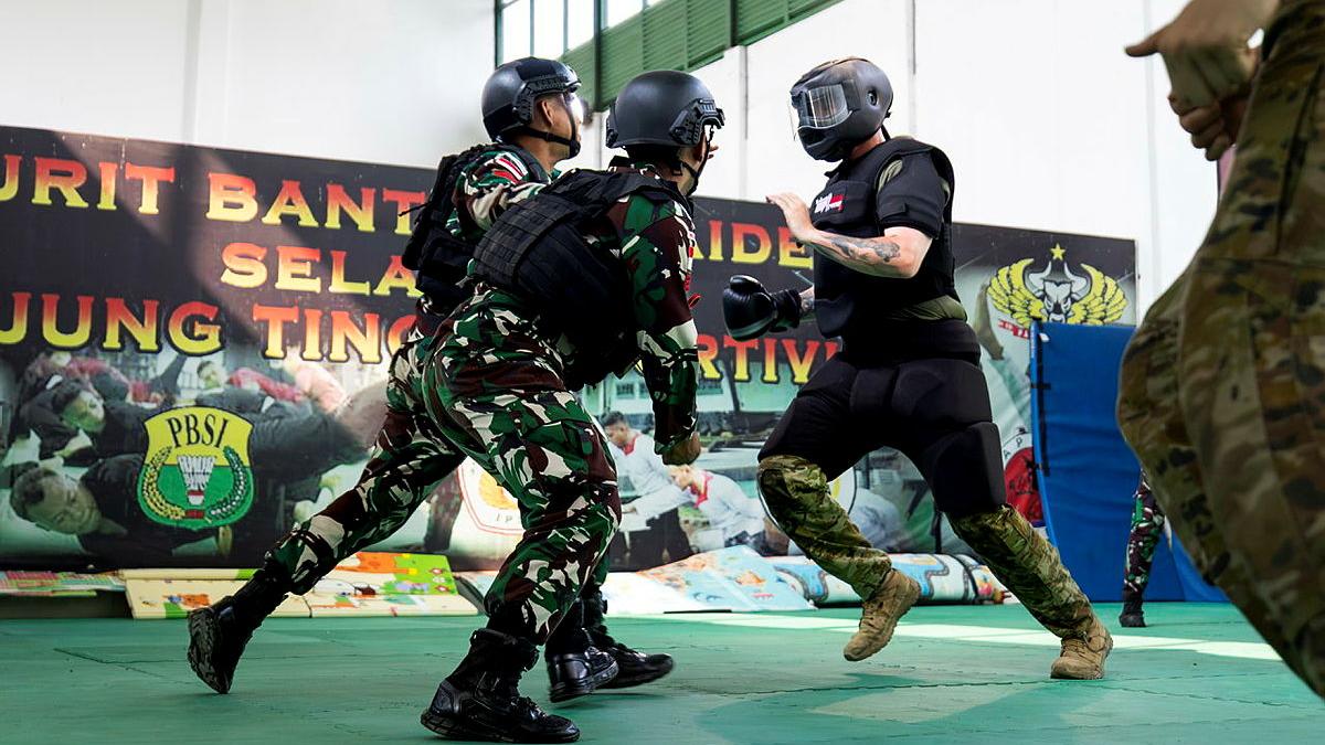 Three people in uniform and helmets assume combat stances.