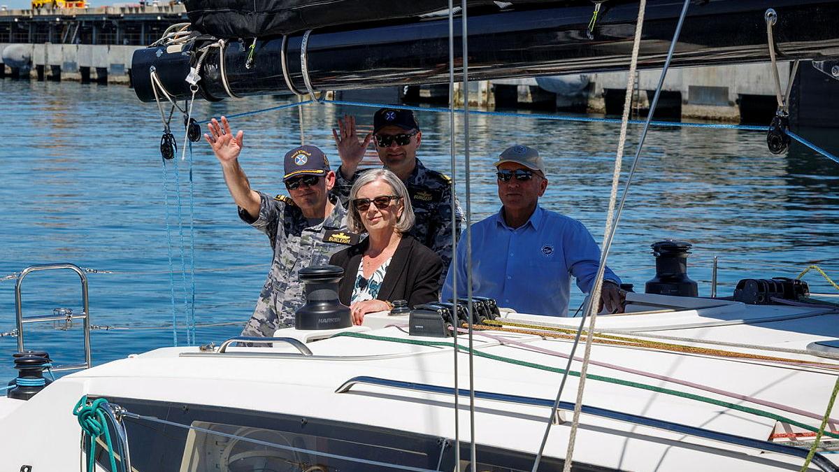 Four people, two in Navy uniforms, sit on a boat and wave.