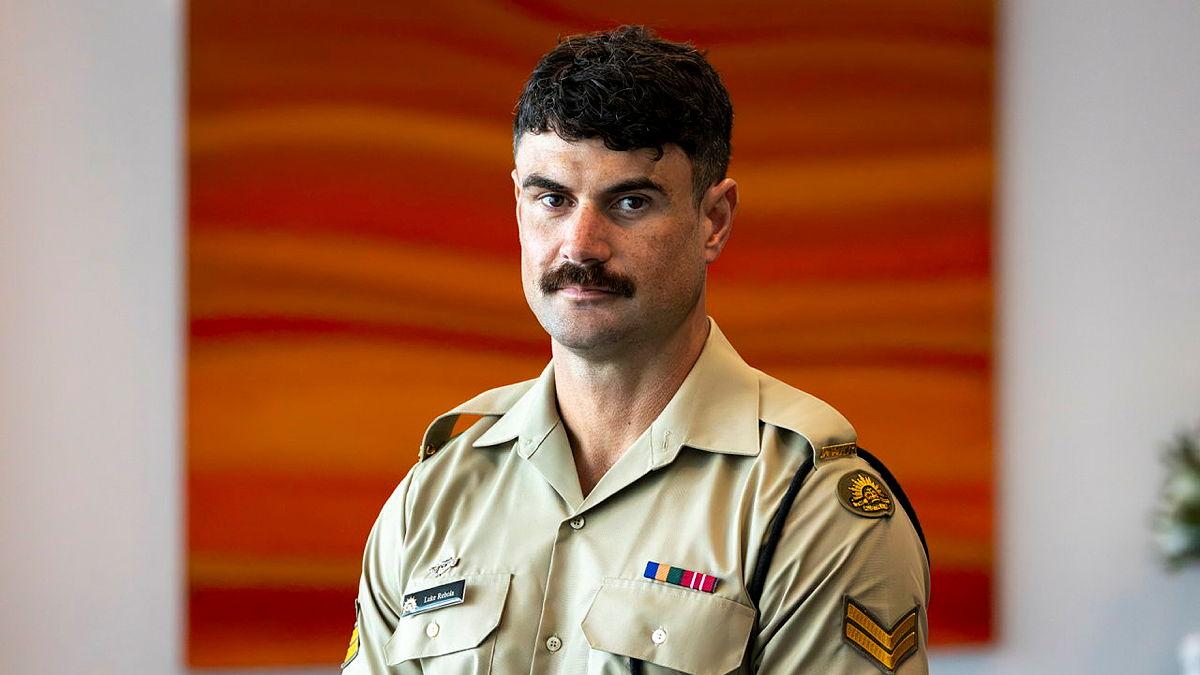 A man in Army uniform stands in front of a red and orange painting. 