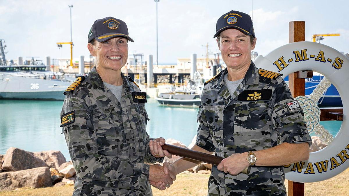 Two women in uniform shake hands while passing a baton between each other.