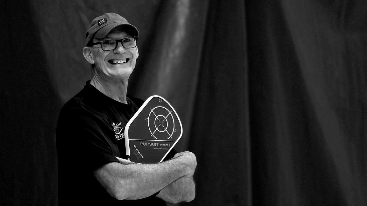 A man wearing a baseball cap and T-shirt hugs a trophy.